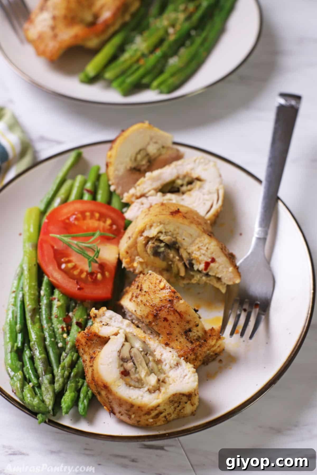 A white plate with stuffed chicken breast cut into pieces with some asparagus and tomato in the plate as well.