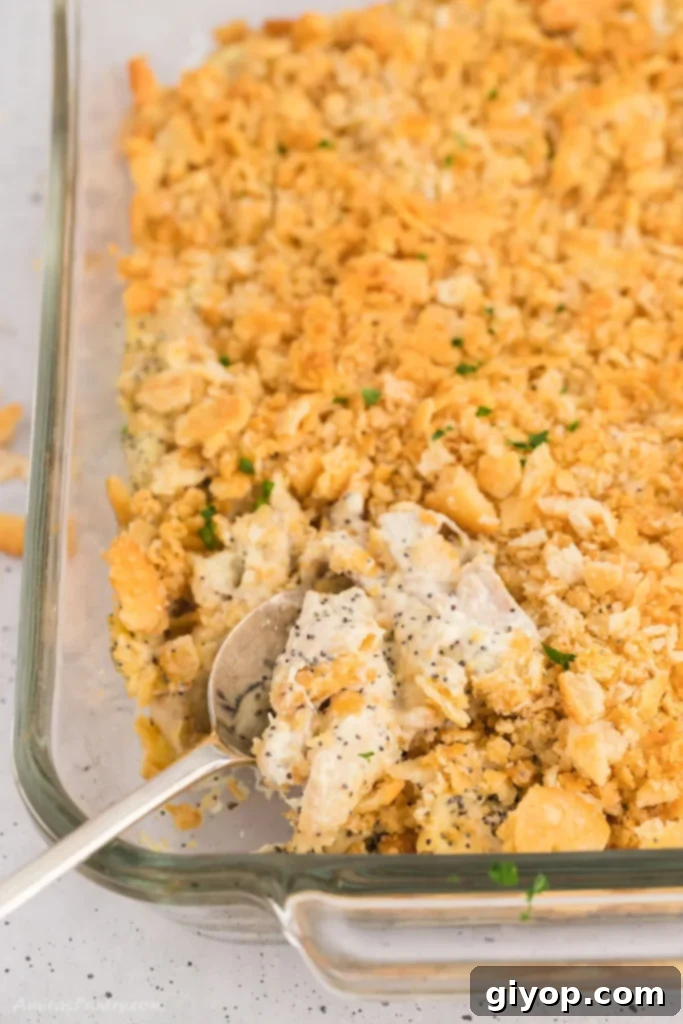 34 Diverse Meal Plans 6 A top-down perspective of a golden-brown poppy seed chicken casserole, complete with a serving spoon nestled within its creamy depths.