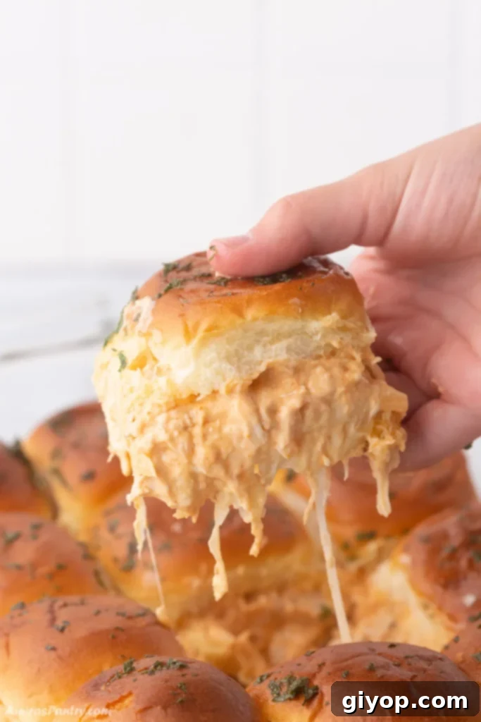 A hand holding a perfectly assembled buffalo chicken slider, showcasing the vibrant ingredients.