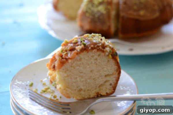 A close-up of a slice of moist yogurt cake with toffee sauce and crushed nuts on a plate, ready to be enjoyed with a fork
