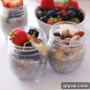 Three jars of chia pudding on a white surface, garnished with fresh fruits and nuts.