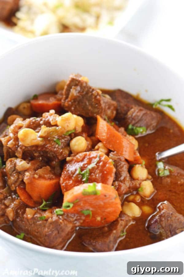 37-Day Meal Blueprint 3 A rustic white bowl filled with a rich and hearty beef stew, featuring tender beef, sweet carrots, wholesome chickpeas, and a vibrant sprinkle of fresh chopped parsley.