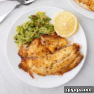 A bird's eye view of a plate with tilapia and some veggies.