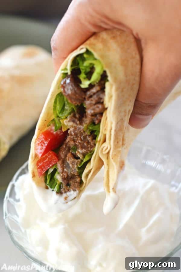 40 Healthy Meal Ideas 5 A hand holding a perfectly wrapped beef shawarma sandwich, with a vibrant garlic sauce for dipping.
