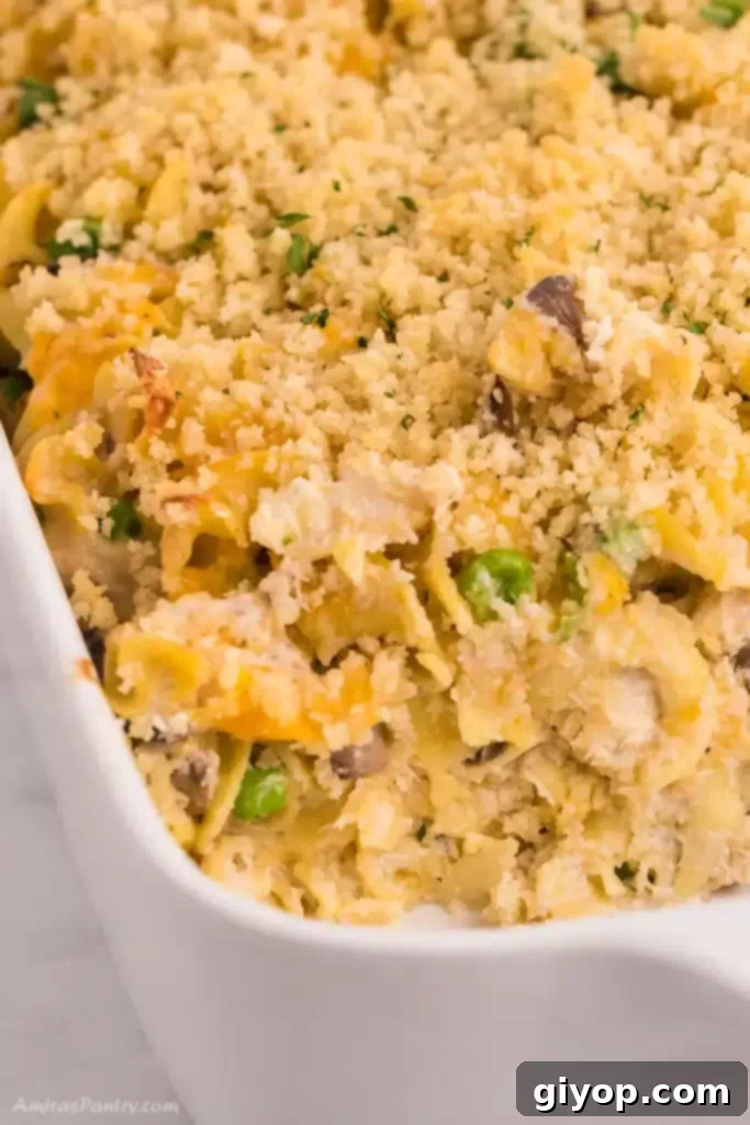 A side view of a golden-brown tuna noodle casserole, with a serving spoon removing a portion, revealing the creamy interior.