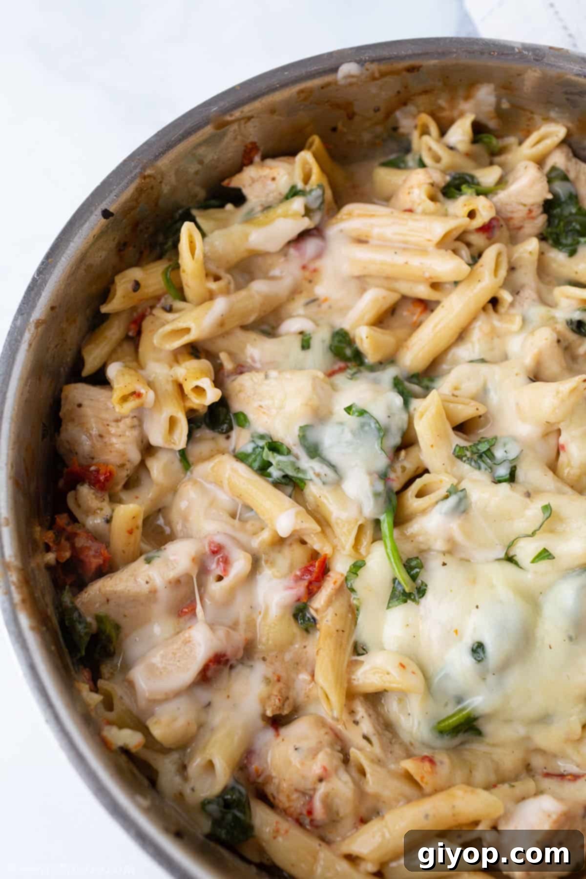 A top-down view of a steaming skillet filled with creamy Tuscan chicken pasta, featuring tender chicken pieces, sun-dried tomatoes, and fresh spinach.
