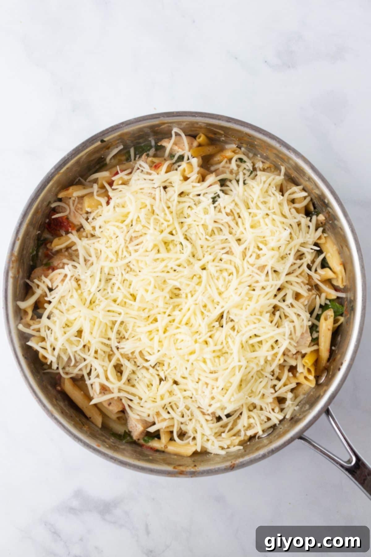A close-up view of a skillet filled with bubbling, cheesy Tuscan chicken pasta, freshly baked and ready to serve.