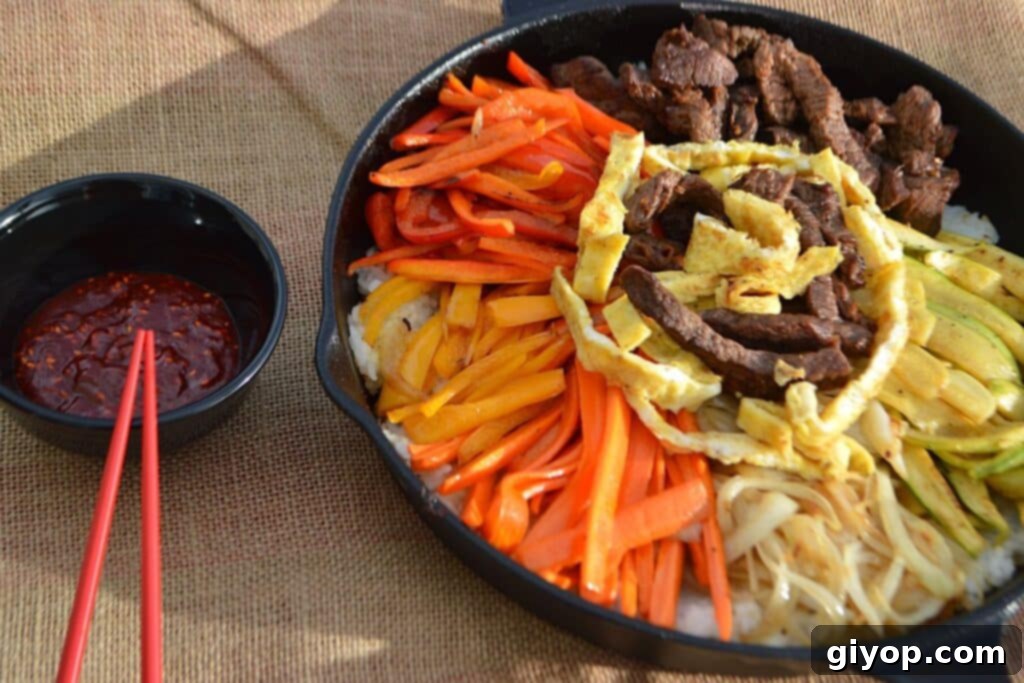 A sizzling skillet filled with colorful Korean Bibimbap, topped with a fried egg and various fresh vegetables.