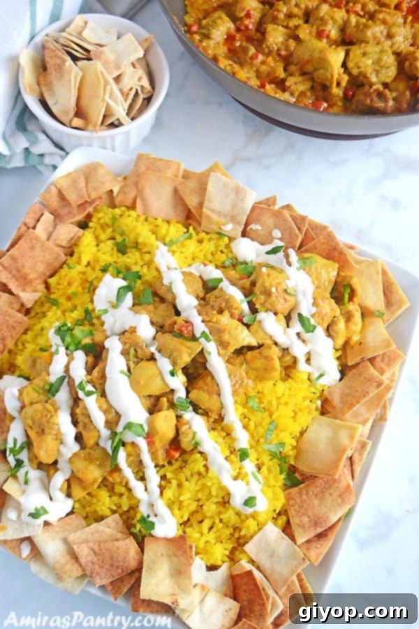 A generous serving of Chicken Shawarma Fatteh on a white platter, featuring seasoned chicken, rice, yogurt sauce, and toasted pita bread.
