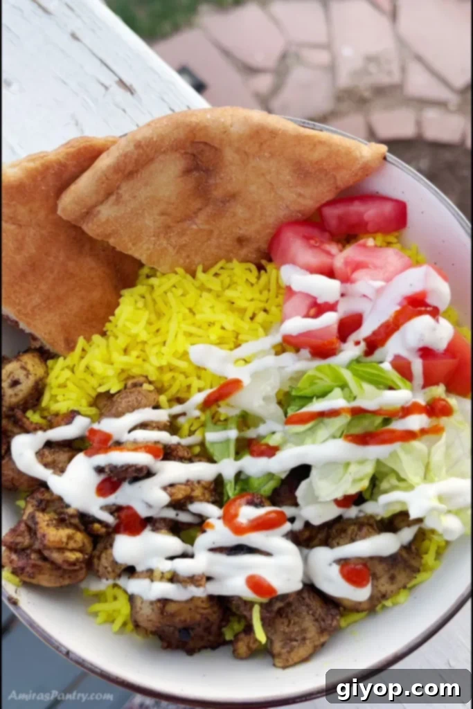 An appetizing overhead view of a Halal chicken and rice bowl, generously topped with white sauce and hot sauce.