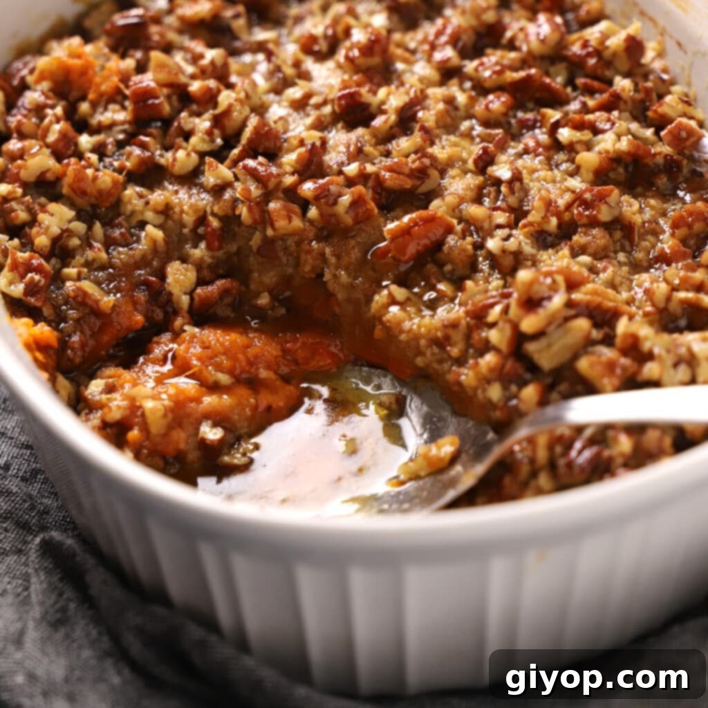 Close-up of a spoon digging into a serving of Sweet Potato Crunch, revealing its layers of soft sweet potato and crunchy topping.