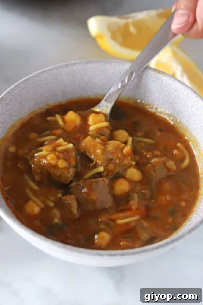 a hand holding a spoon and scooping some harira soup of a grey bowl.