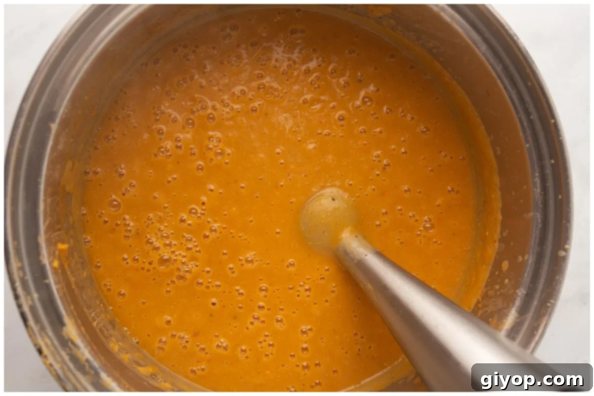 An immersion blender blending soup in a pot. 