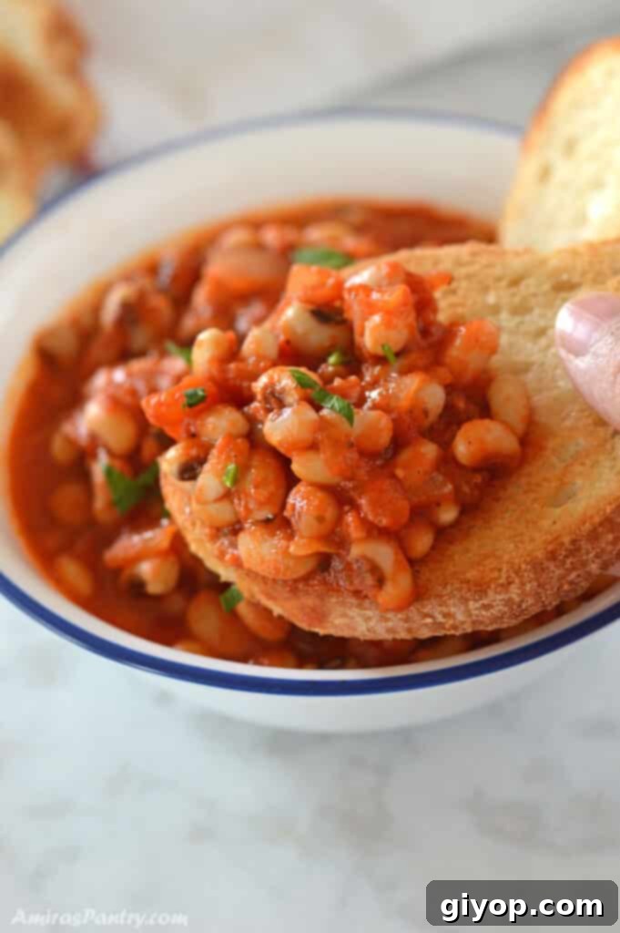 A hand holding a piece of bread scooping some black peas stew, highlighting its rich texture.