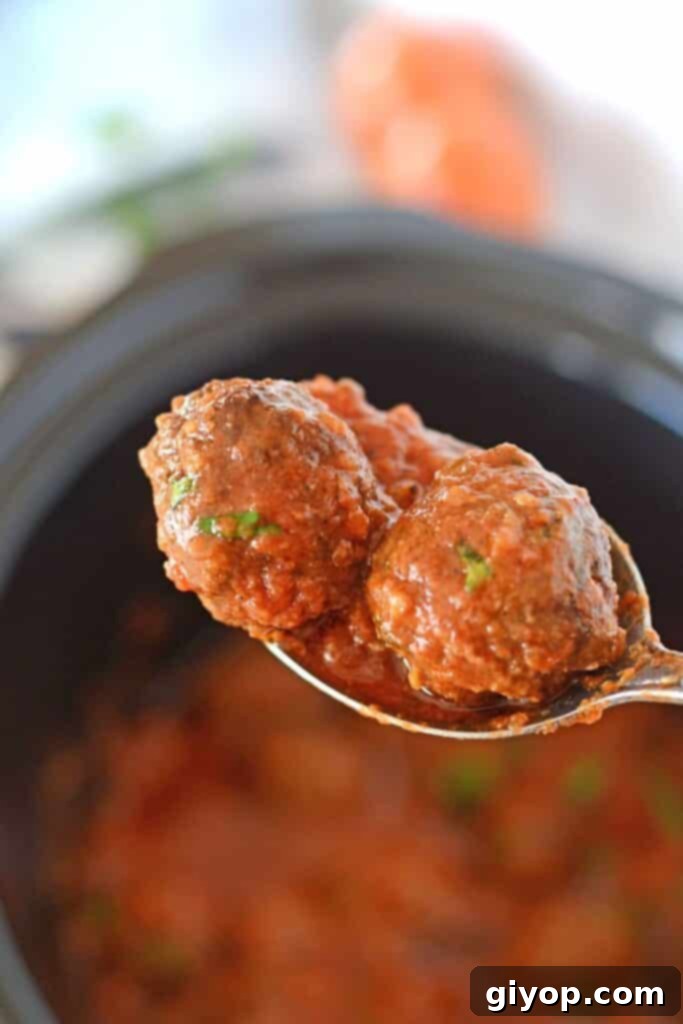 A close-up view of a spoon scooping tender meatballs from a slow cooker, emphasizing their saucy appeal.