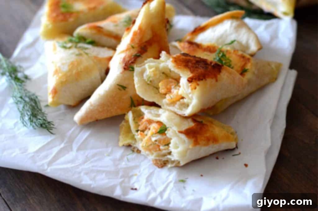 Baked samosas arranged on parchment paper, with one cut open to reveal the creamy dill shrimp filling.