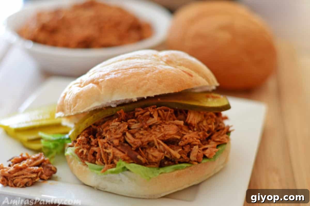A delicious pulled BBQ chicken sandwich alongside a bowl of shredded chicken, ready to be served.