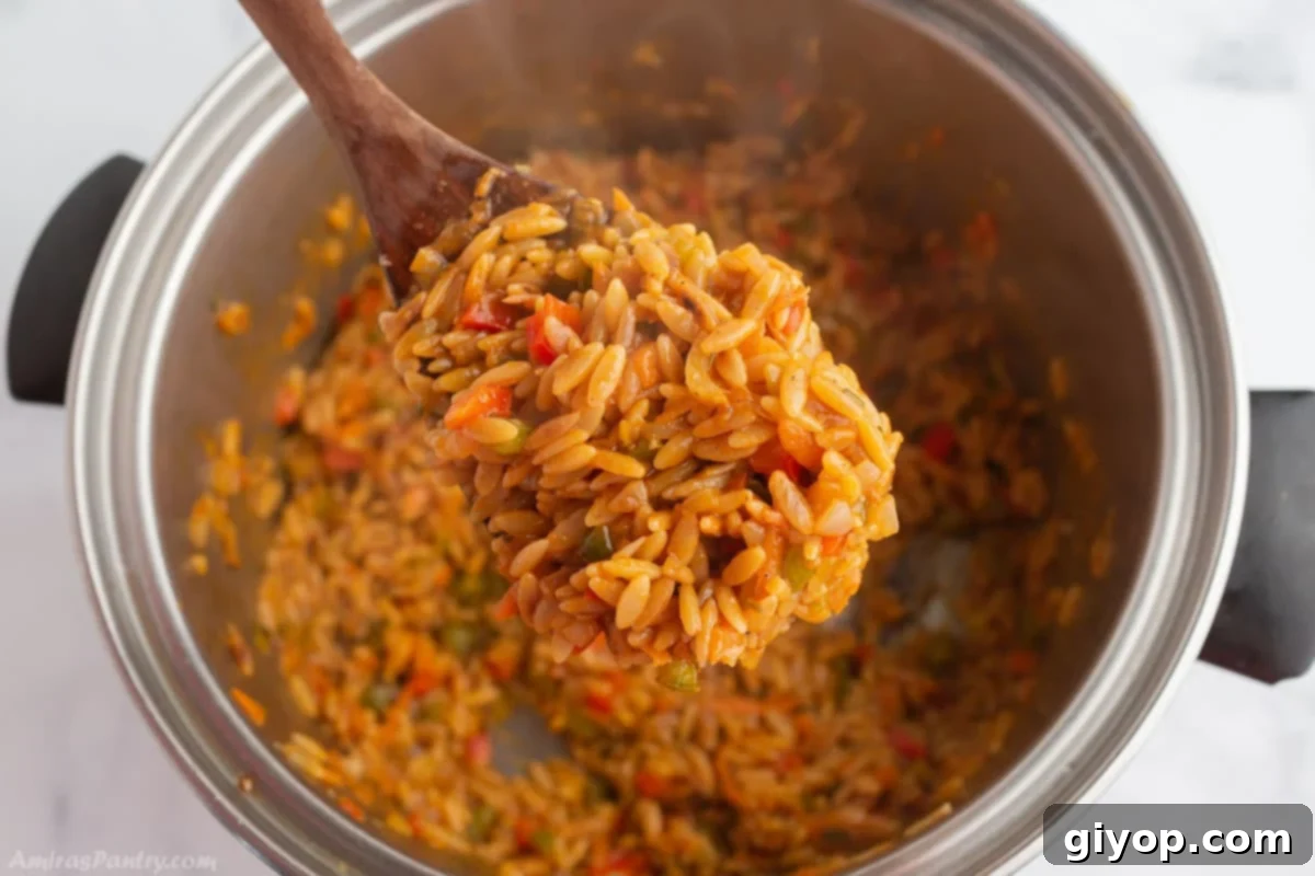 A wooden spoon scooping a generous portion of vegetarian orzo from a large cooking pot, highlighting the creamy texture and colorful vegetables of the dish.