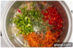 Diced bell peppers, grated carrot, garlic, and fresh rosemary added to sautéed onions in a pot.