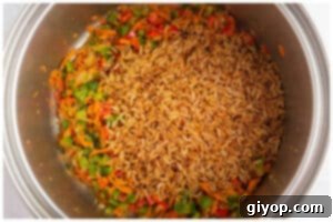 Toasted orzo mixed with colorful sautéed vegetables in a pot, ready for the liquid.