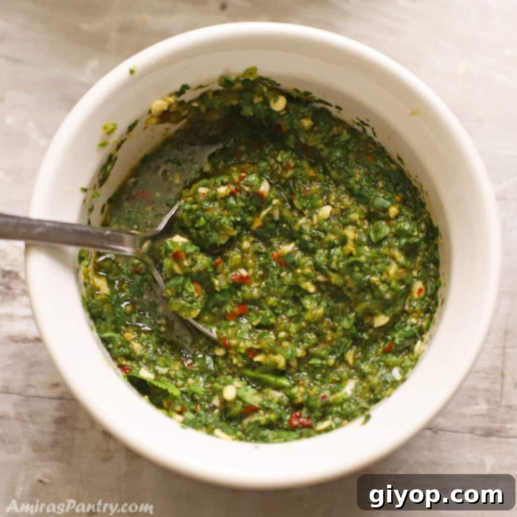 A small bowl holding a vibrant green Zhoug sauce, with a spoon resting within, indicating its readiness to be served.