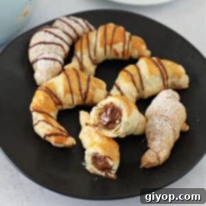 chocolate croissants on a black plate with one cut in half.
