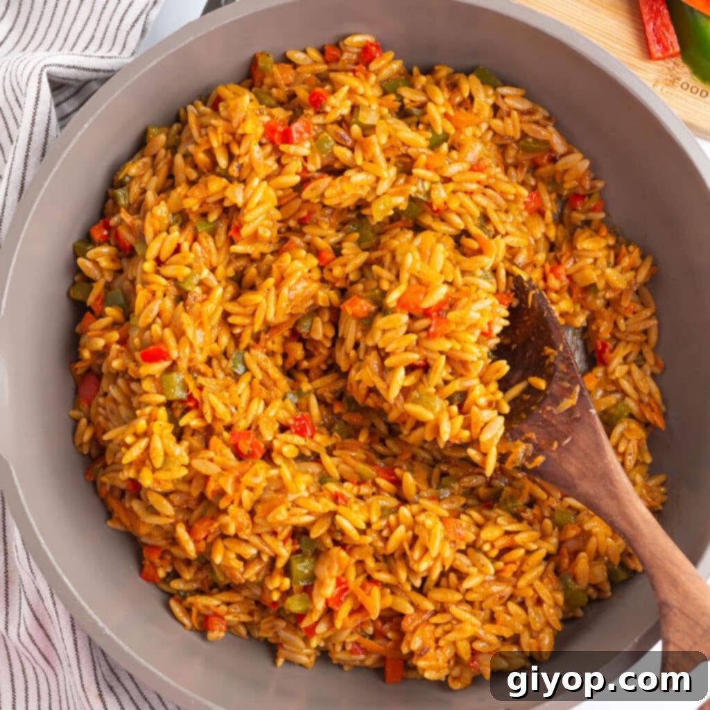 A large skillet of orzo with colorful vegetables and a wooden spoon, ready to be served.