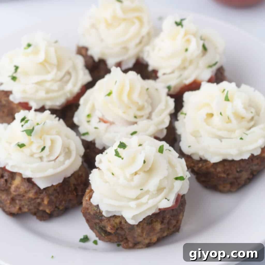 Mini meatloaf cupcakes topped with a savory 'frosting' and fresh herbs on a rustic wooden board.