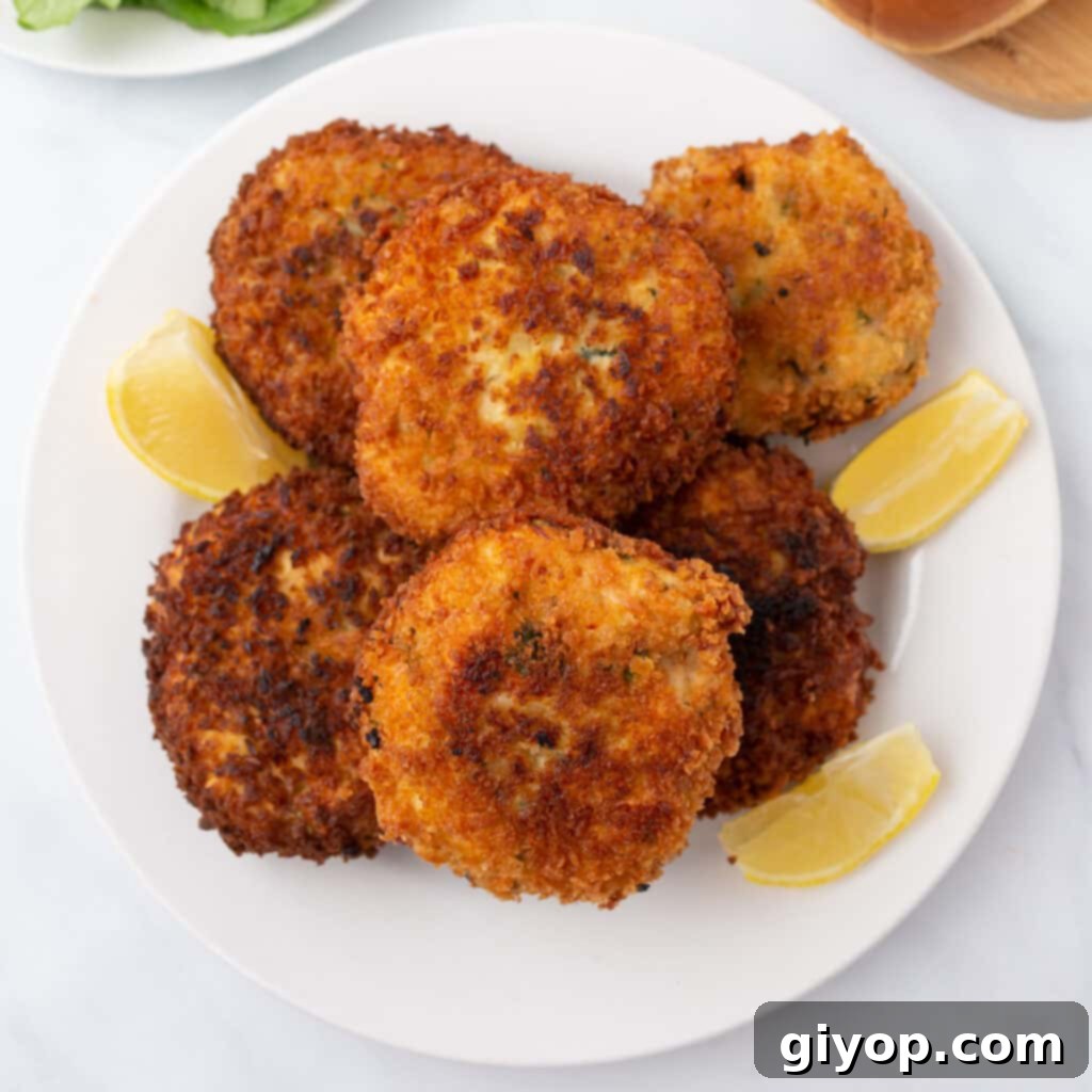 A top view of golden-brown chicken patties arranged neatly on a white dish with bright lemon wedges.