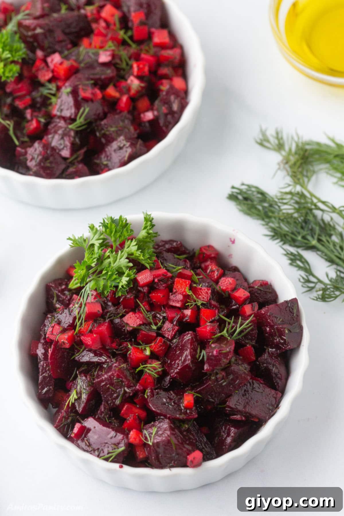 An overhead view of two white bowls of beet salad, garnished with fresh dill.