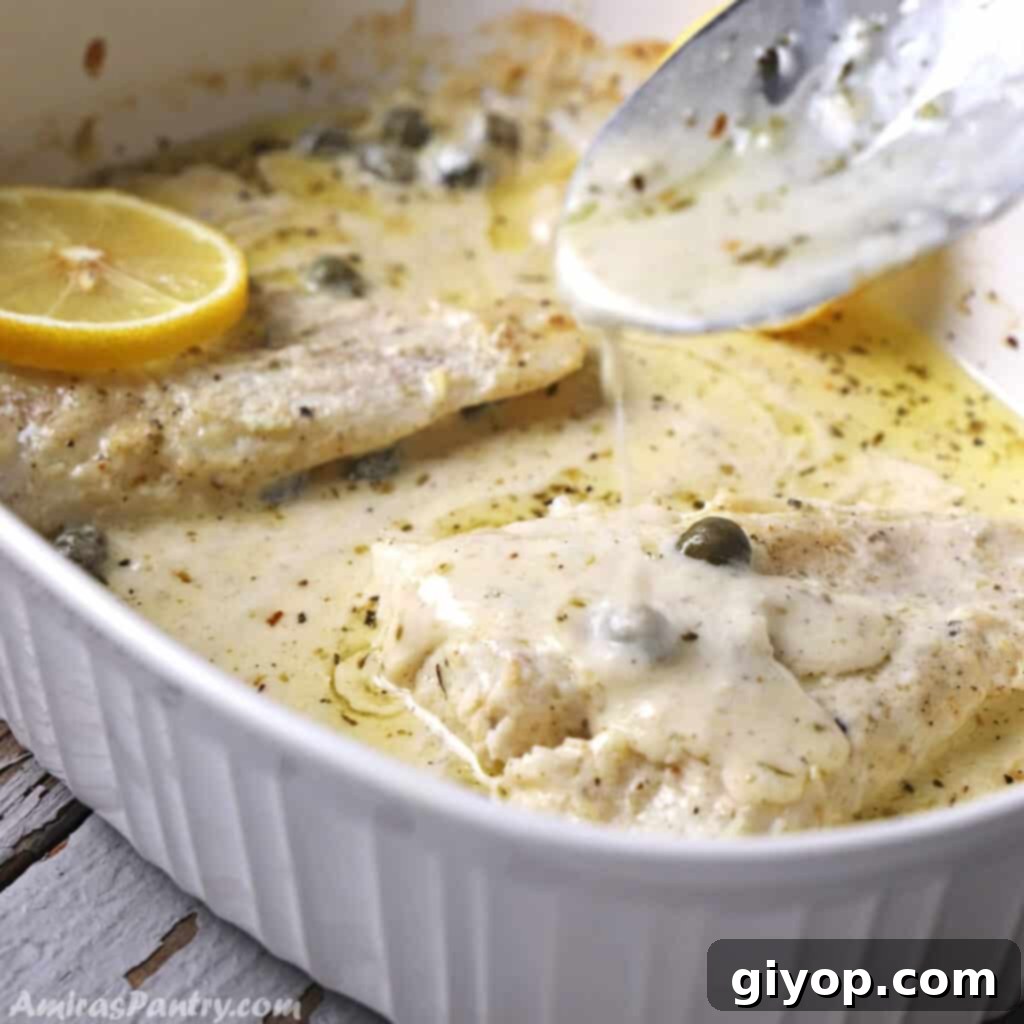 A spoon scooping some creamy lemon sauce over perfectly baked fish fillet in a white pan, ready to serve.