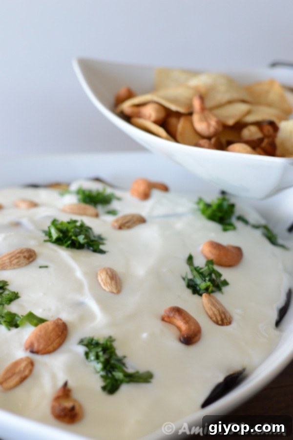 A close-up of the creamy yogurt topping on Eggplant Fatteh, garnished with nuts.