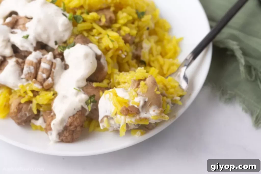 A spoon scooping some flavorful chicken shawarma rice from a plate, highlighting the delicious texture and ingredients.