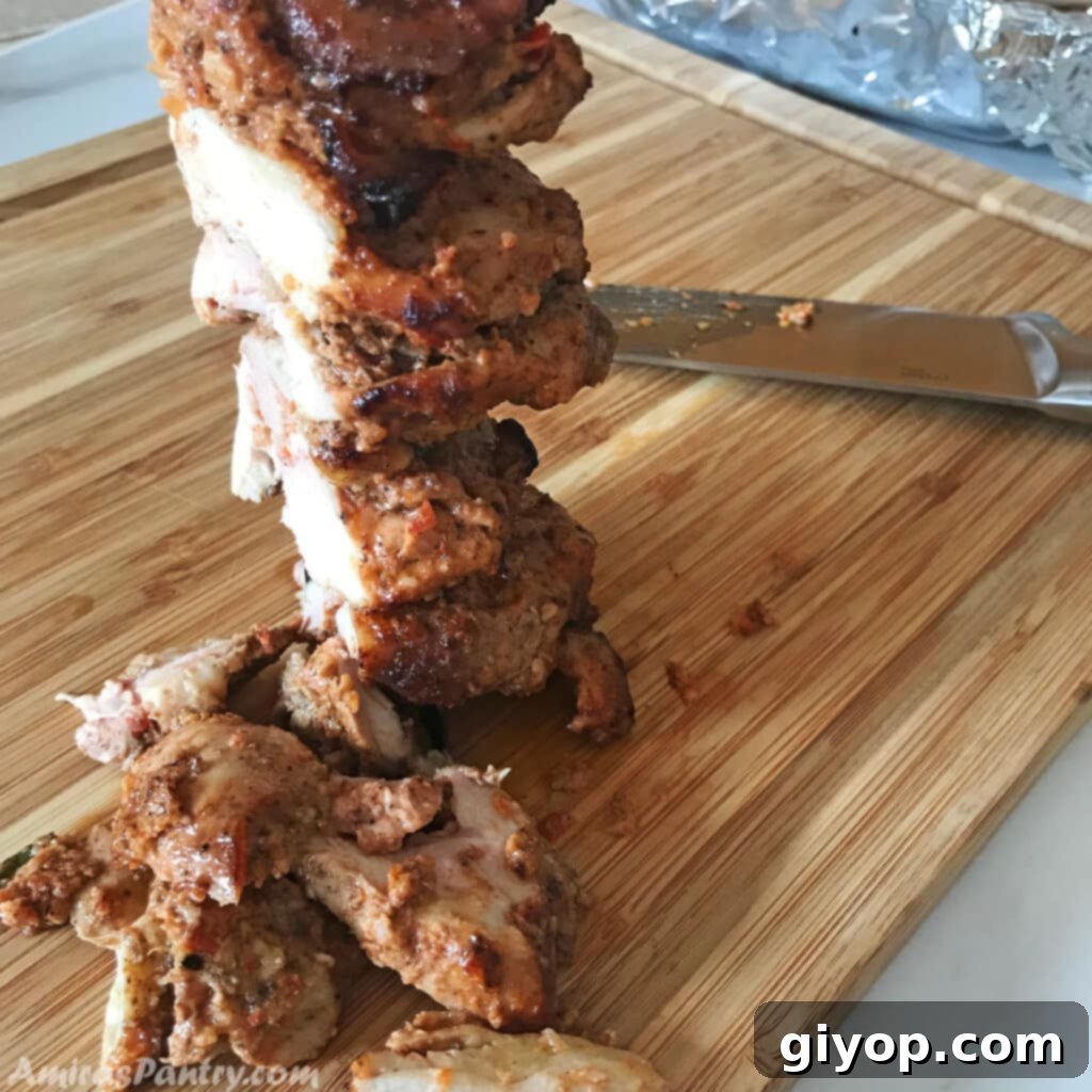 Close-up of succulent chicken shawarma meat being carved on a rustic wooden surface, ready for serving.