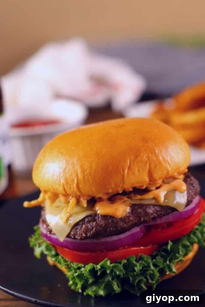 A juicy hamburger sandwich generously topped with crisp lettuce, melted cheese, ripe tomatoes, and a hint of ketchup in the background.