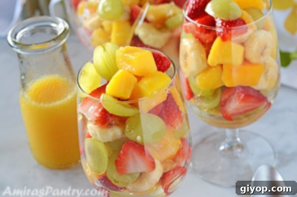 Two clear cups filled with vibrant mango fruit salad, with an orange dressing in the background.