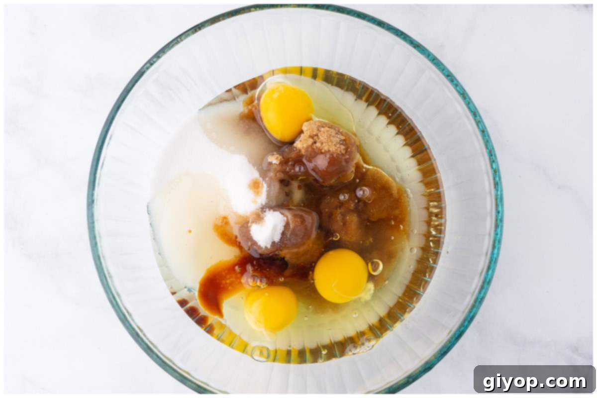A close-up of eggs, sugar, and oil being beaten together in a mixing bowl until light and creamy.