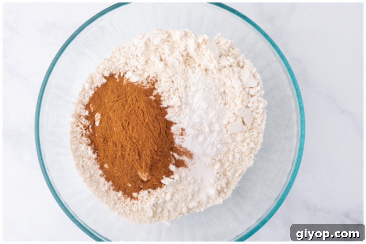 A bowl containing the dry ingredients for the cake, including flour, cinnamon, baking soda, baking powder, and salt, whisked together.