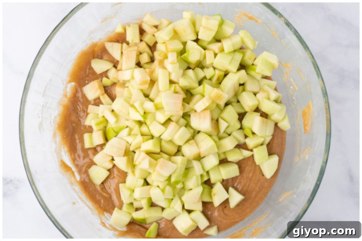 A bowl of cake batter mixed with generous apple cubes, showcasing the texture before baking.