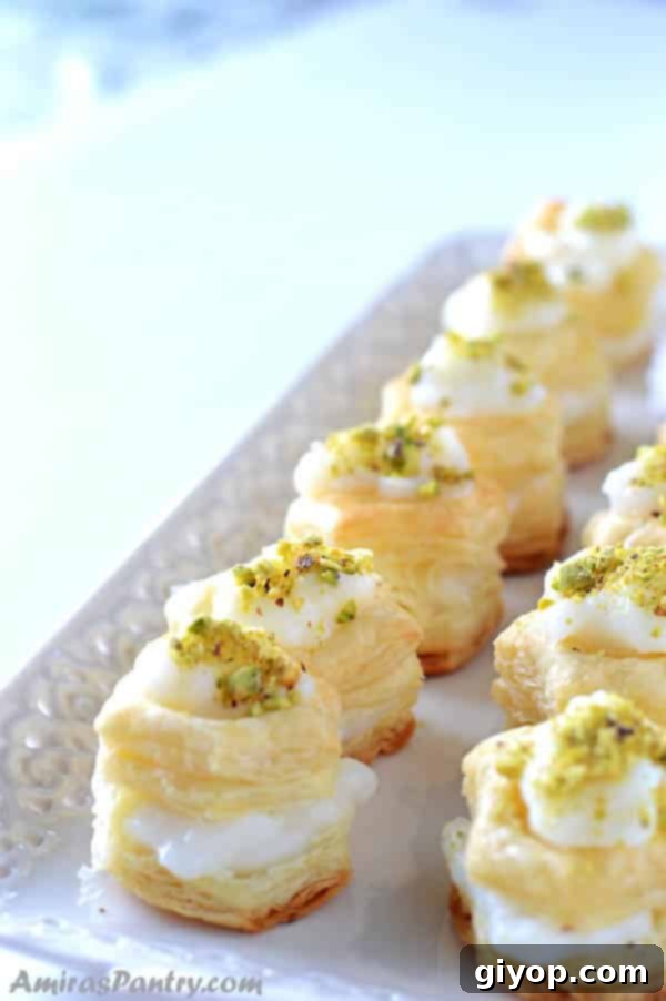 Shaabiyat: The Middle East's Golden Flaky Treat 3 two rows of puff pastry squares filled with cream, garnished with pistachios and placed on a white serving platter.