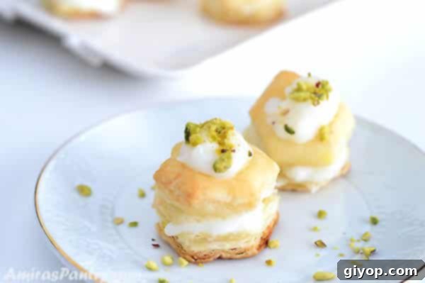 Shaabiyat: The Middle East's Golden Flaky Treat 5 Two puff pastry squares stuffed with cream and garnished with pistachios on a small white dessert plate with golden rim.