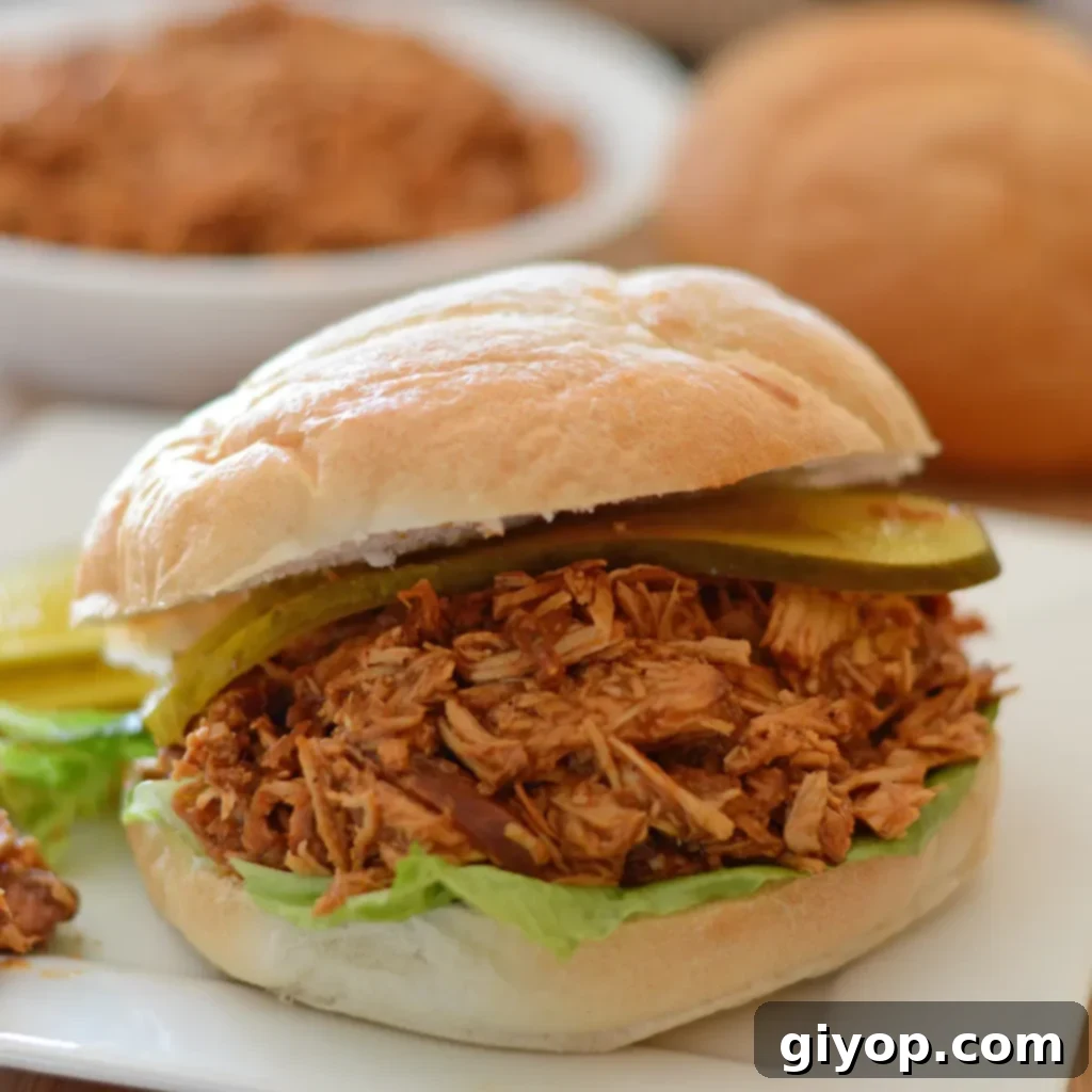 Meal Plan 5 A mouth-watering pulled BBQ chicken sandwich served on a white plate, with a large bowl of tender pulled chicken in the background, inviting a delicious feast.