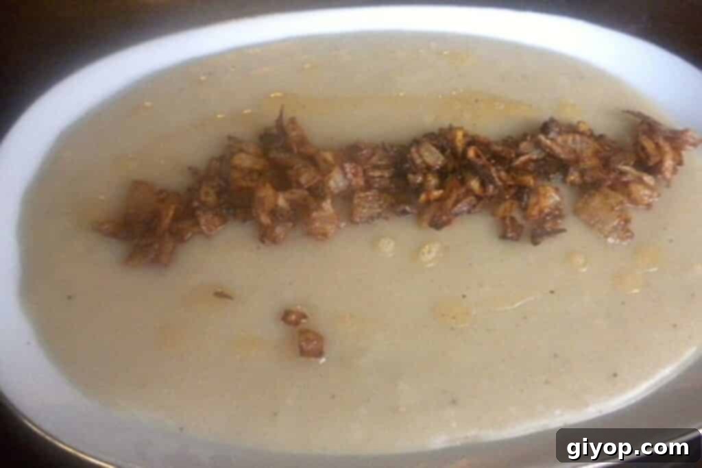 A plate with a creamy dish of kishk, garnished with crispy fried onions and fresh herbs.