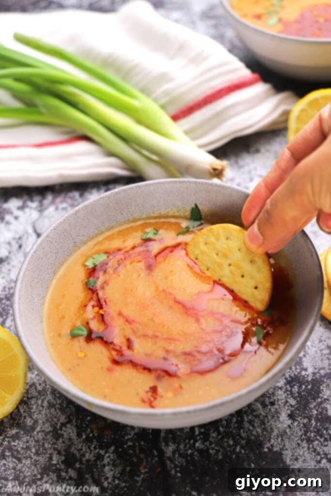 A hand dipping a crispy piece of homemade garlic bread into a bowl of rich, warm Egyptian Lentil Soup, highlighting the comforting textures and inviting aroma of the meal.