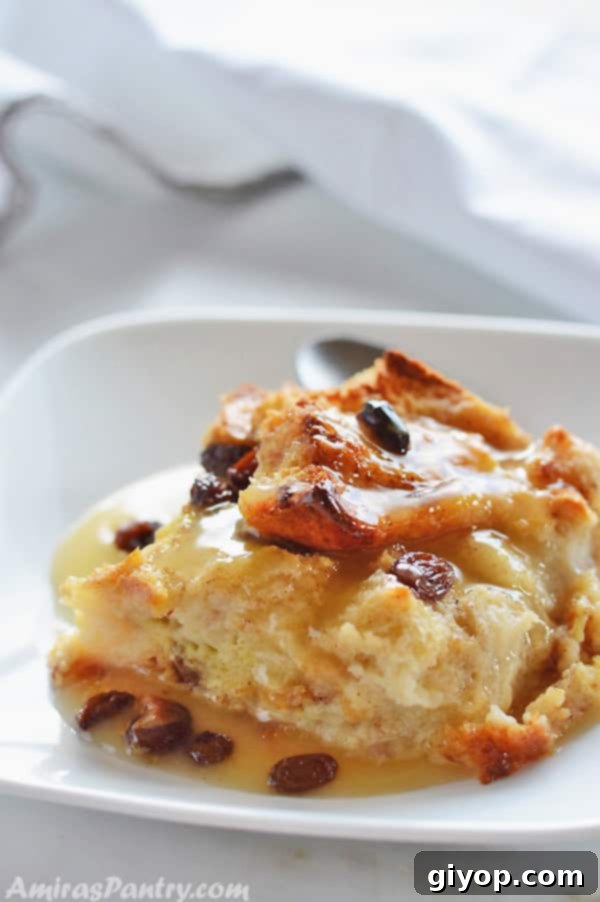 A delectable slice of classic bread pudding, richly textured and studded with raisins, elegantly presented on a pristine white plate, promising a comforting and sweet indulgence.