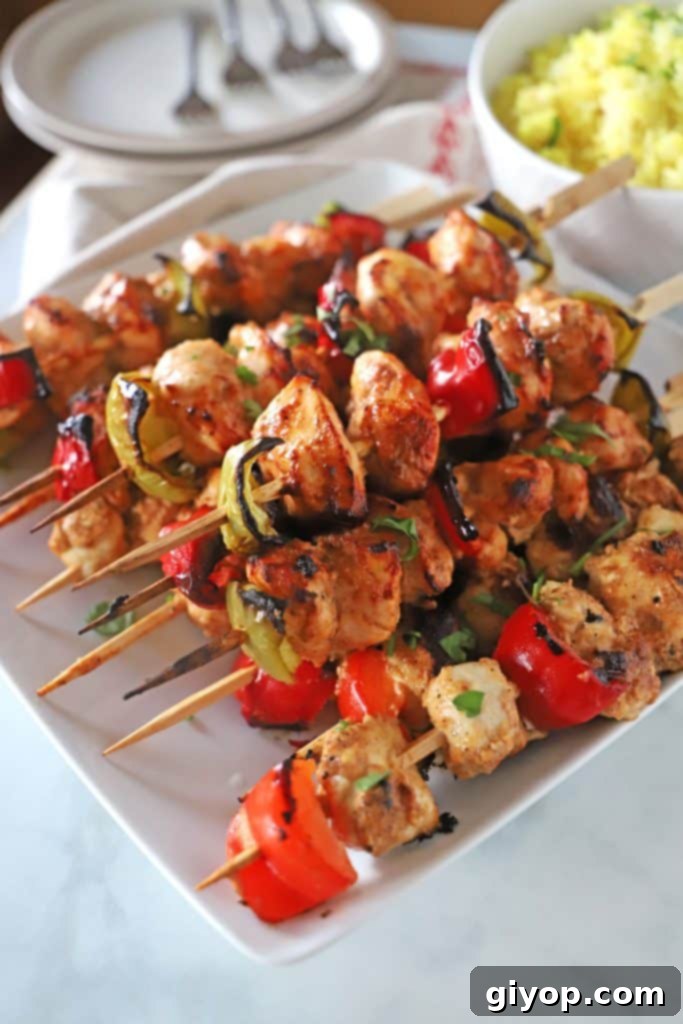Perfectly grilled chicken shish tawook skewers arranged on a white square serving plate, resting on an elegant marble table top.