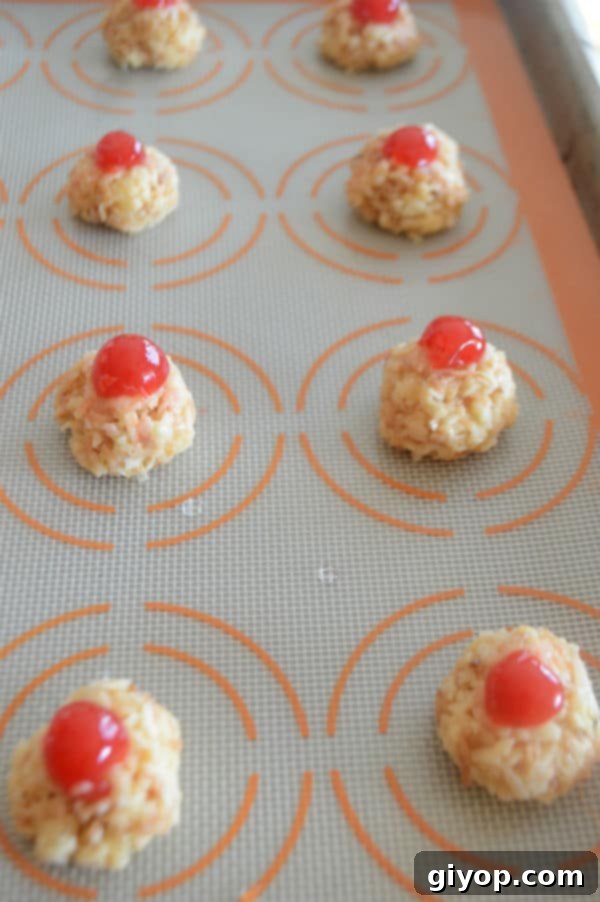 A cooking sheet, with Macaroon balls and a berries, showcasing macaroons topped with candied cherries before baking.