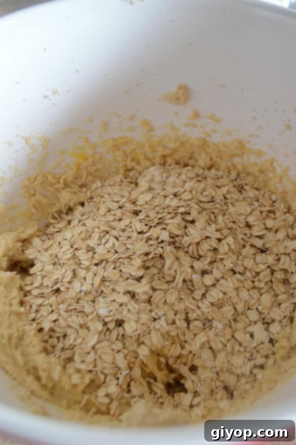 A bowl containing the wet ingredients, with rolled oats being added, ready for mixing