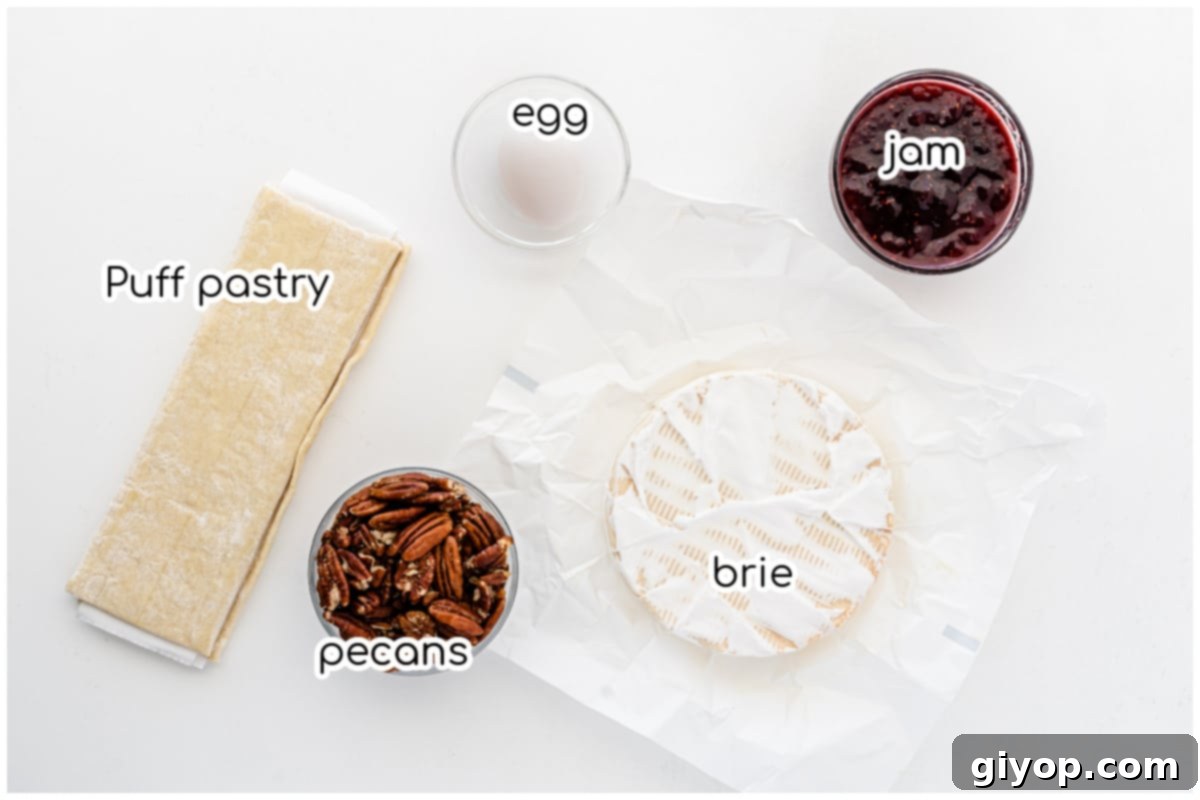 Ingredients for the baked brie recipe: a wheel of brie, puff pastry, raspberry jam, pecans, and an egg for wash.