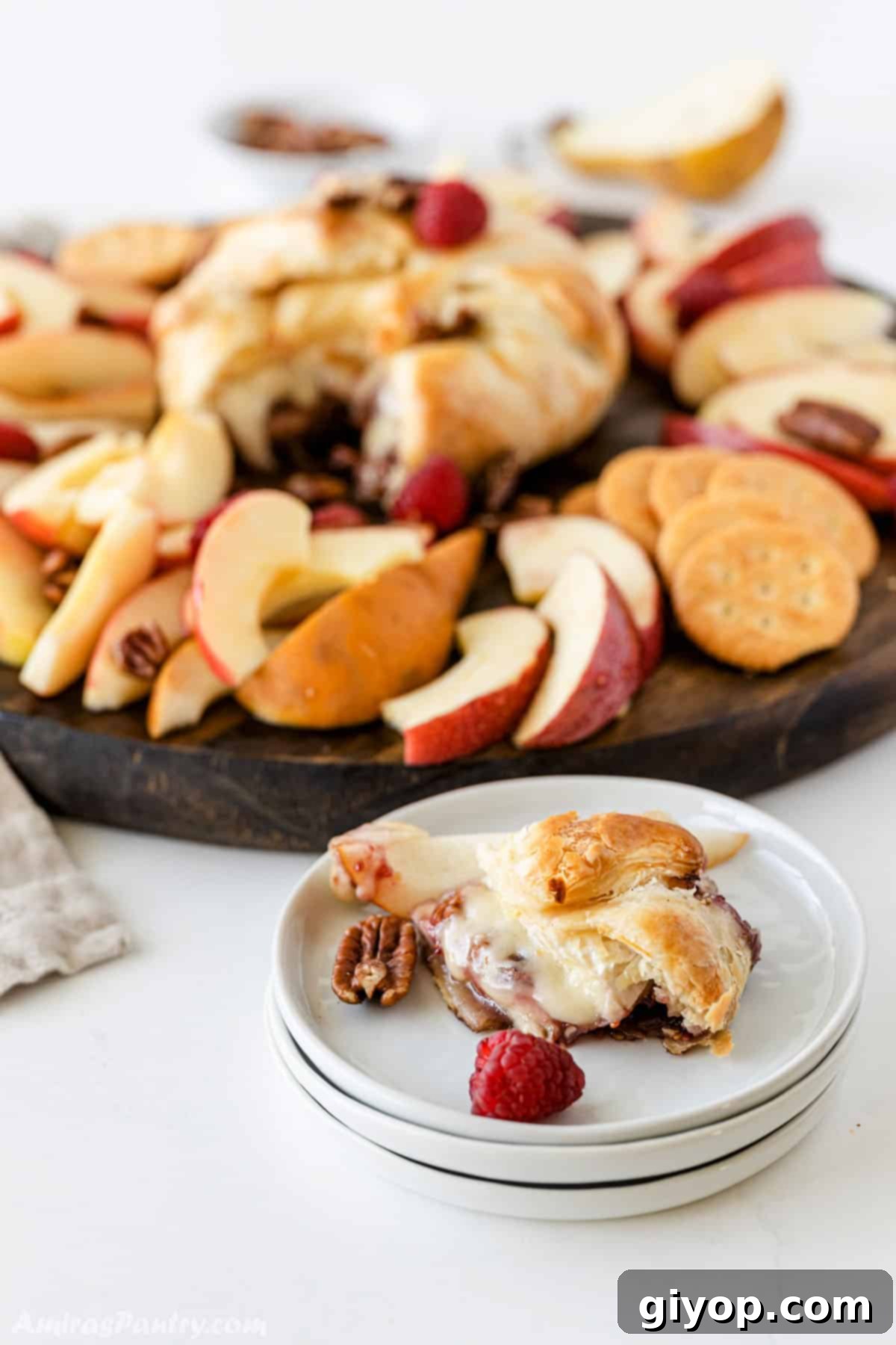 A slice of baked brie in puff pastry on a small white plate with pecan and raspberries, showcasing the gooey center.